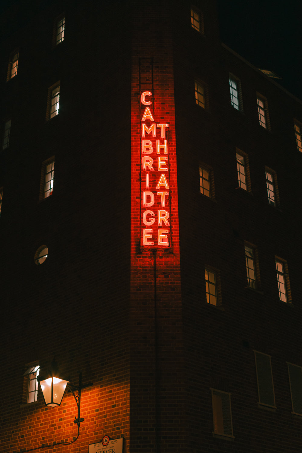 Illuminated Cambridge Theatre neon sign on a brick building at night, photographed by Francois Louw
