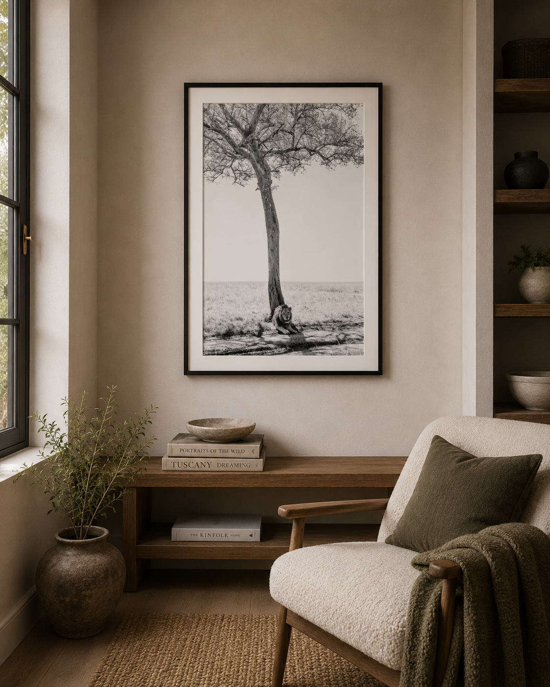 Nestled corner of a room with a framed black and white lion and tree print on the wall, a small wooden table with books and a plant, and a cozy armchair with a blanket.