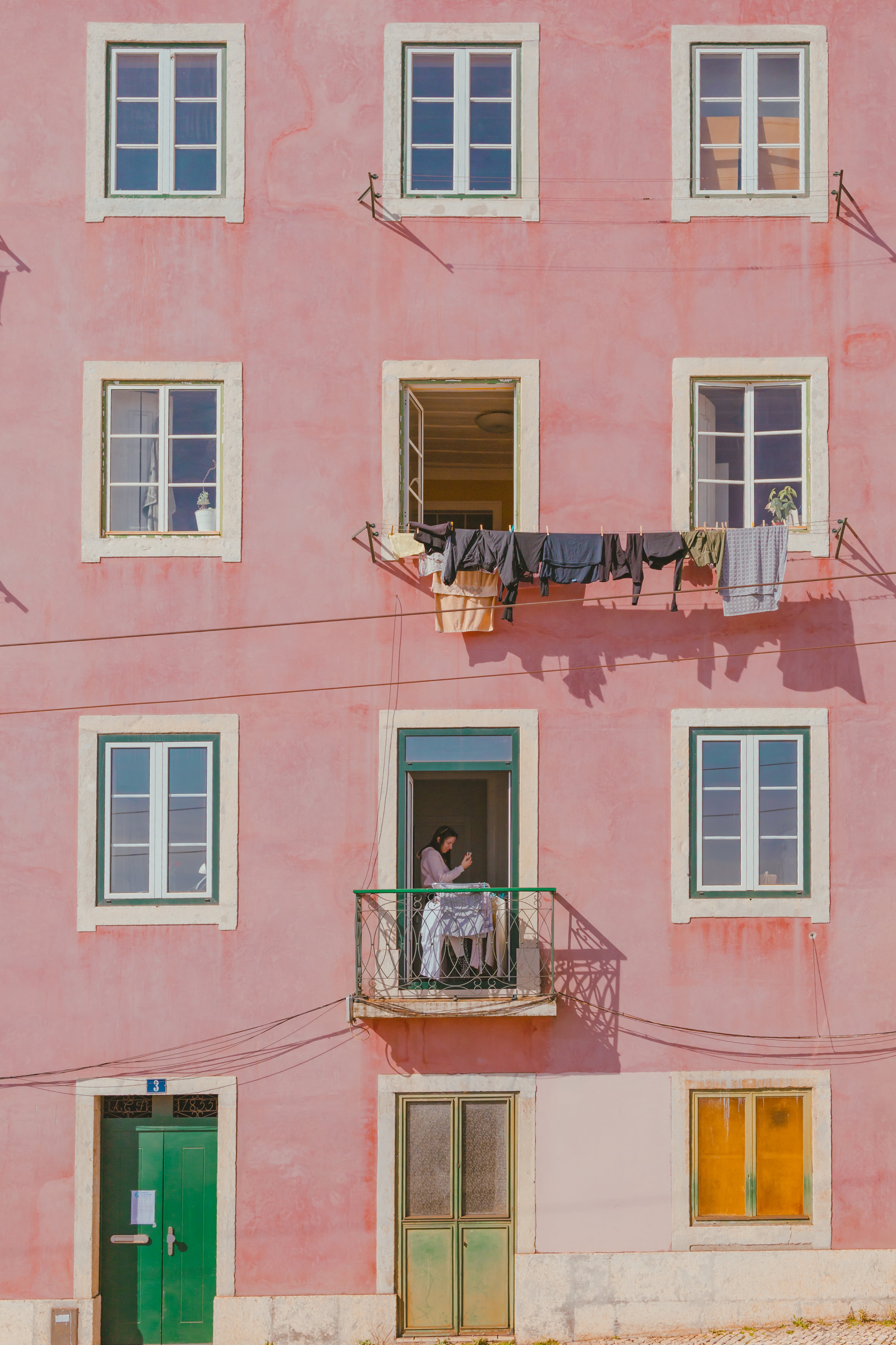 Pink building facade with a woman on a balcony and laundry hanging outside, photographed by Francois Louw