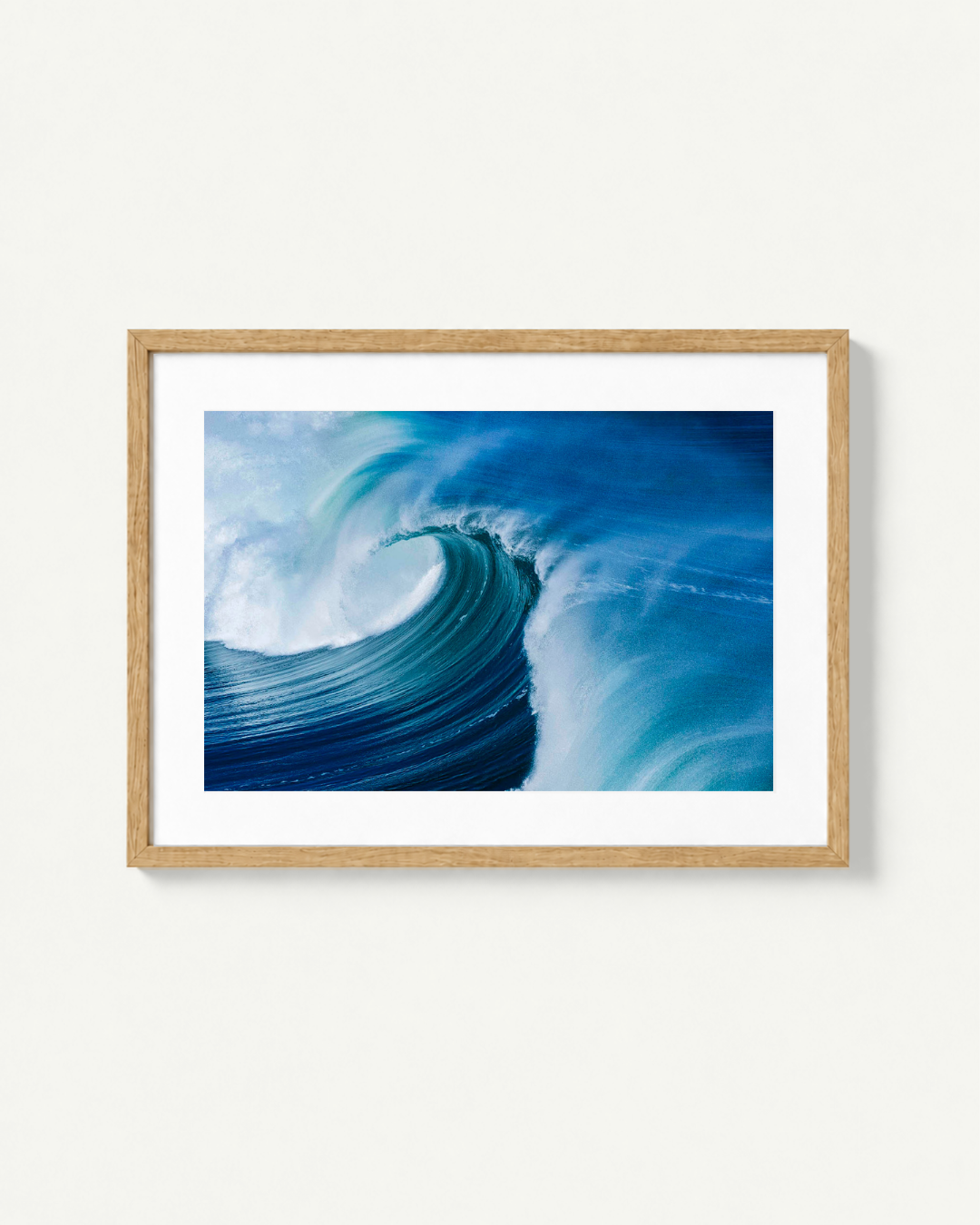 A framed art print of a curling ocean wave in shades of blue and white, set in a light natural wood frame with a white mat, displayed against a clean off-white wall.