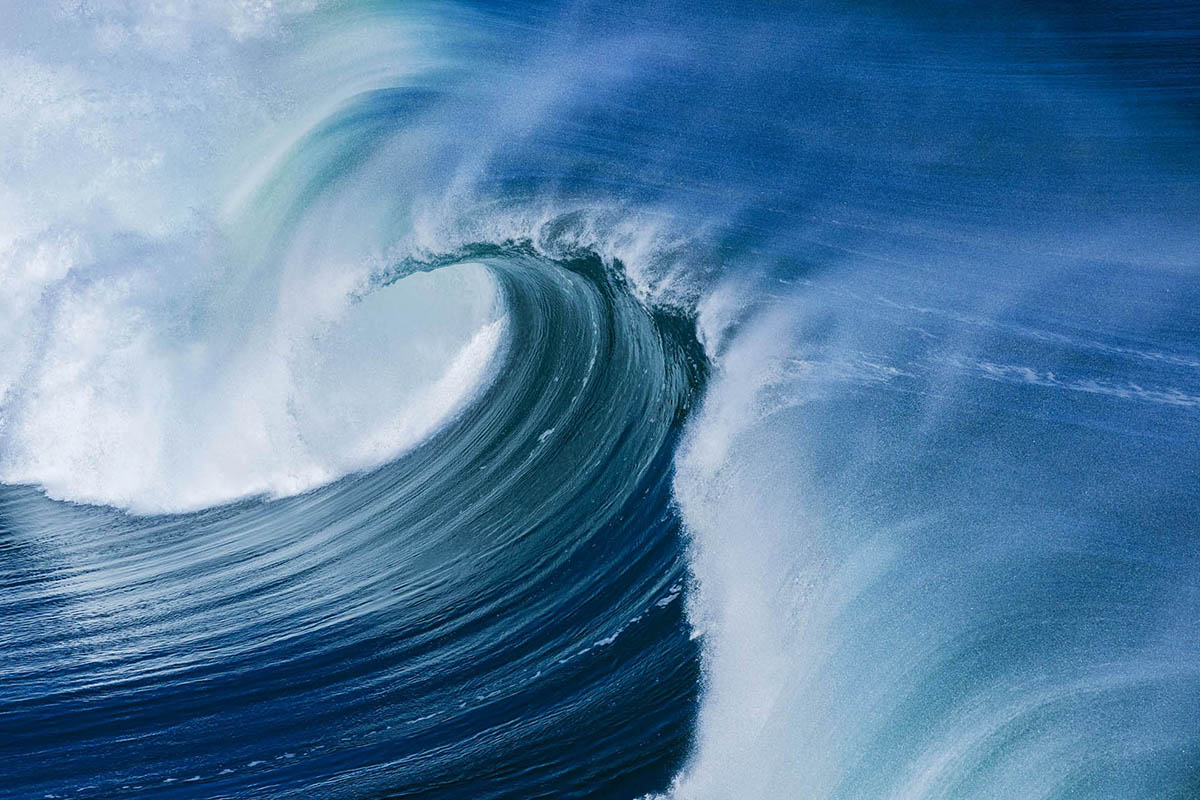 Photograph of a powerful blue ocean wave curling and breaking across the surface of the sea, photographed by Richard du Toit