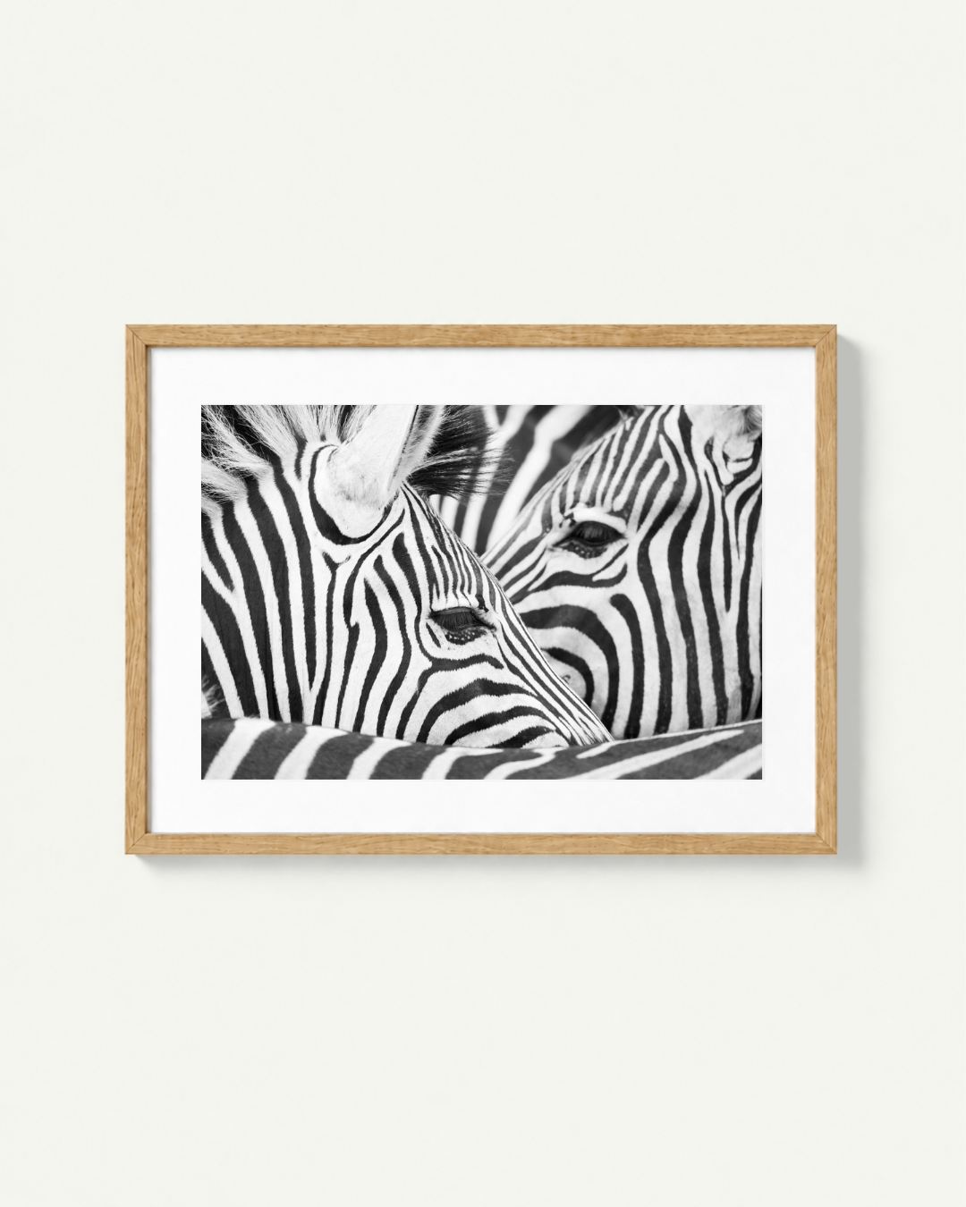 Framed black and white zebra print with a light wood frame and white mat, displayed on a light beige wall.