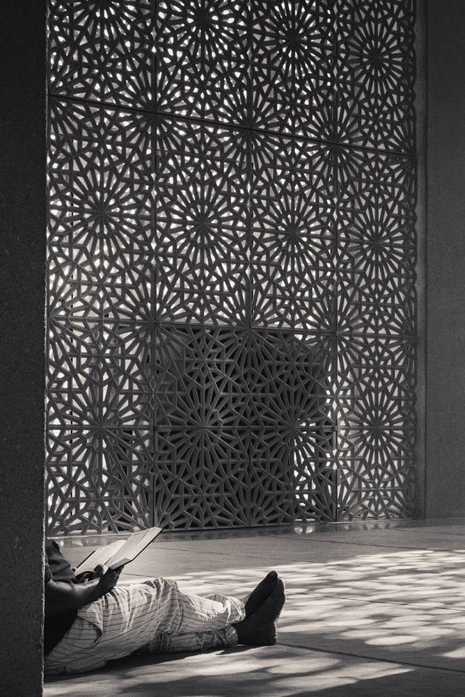 A picture of a man in a place of worship, a mosque, reading holy scripture