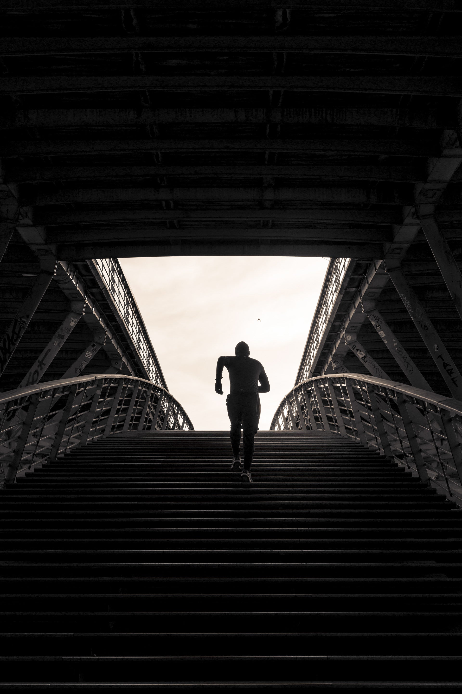 Jogger running up a set of stairs on a bridge with a bright light at the top, photographed by Stef Leny in Paris.